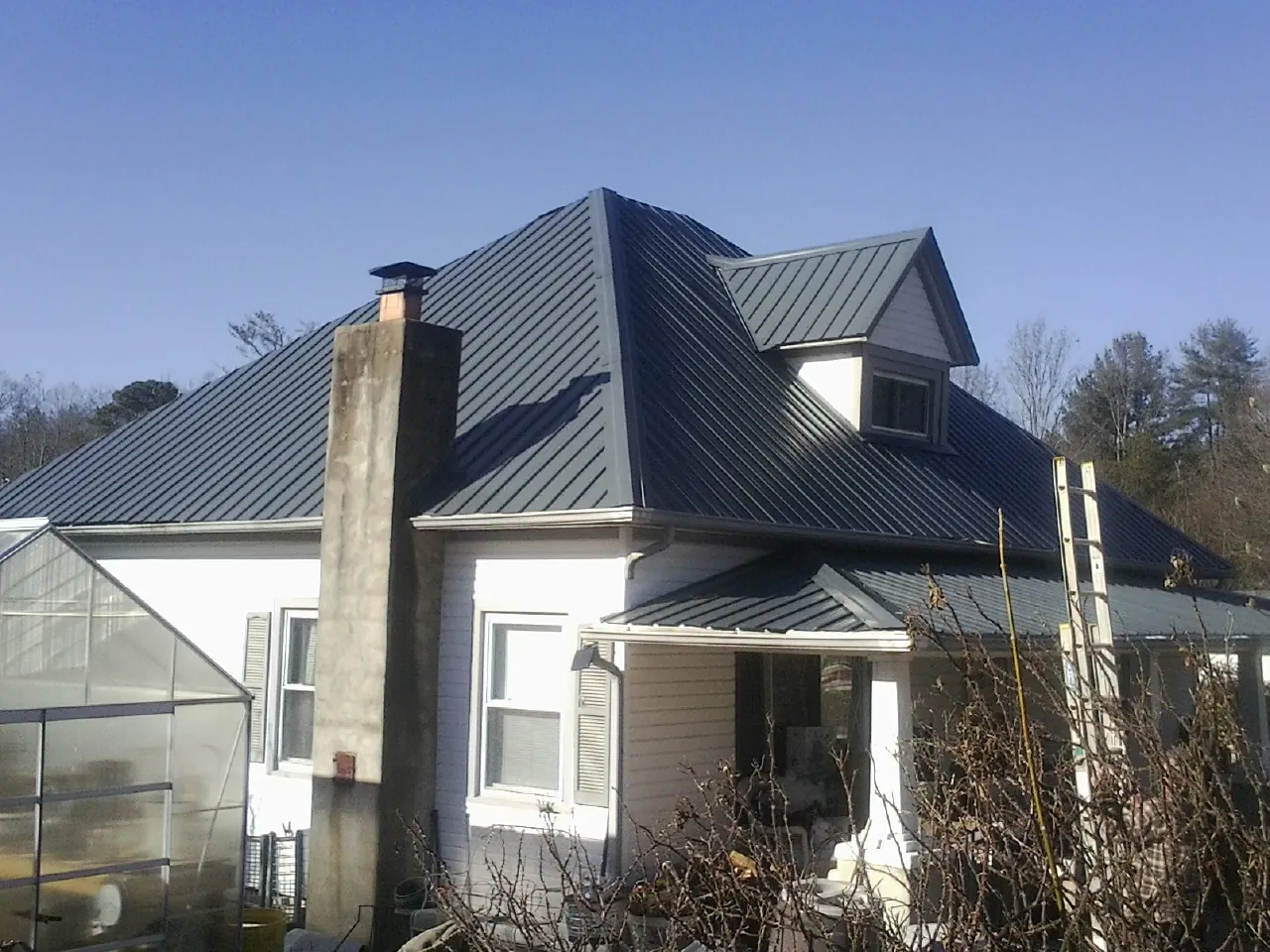 Dark blue standing seam metal roof on a white farmhouse with dormer — Slate & Tile Roof Repair by Roofing Brothers in Zwingle