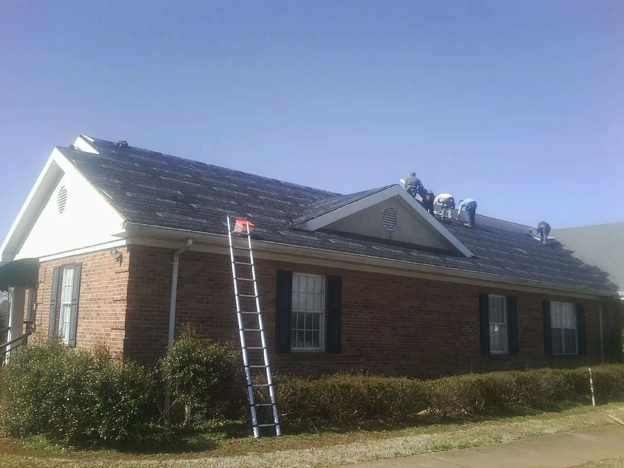 Crew tearing shingles off a brick ranch roof with a ladder set — Emergency Roof Repair work by our crew in Zwingle