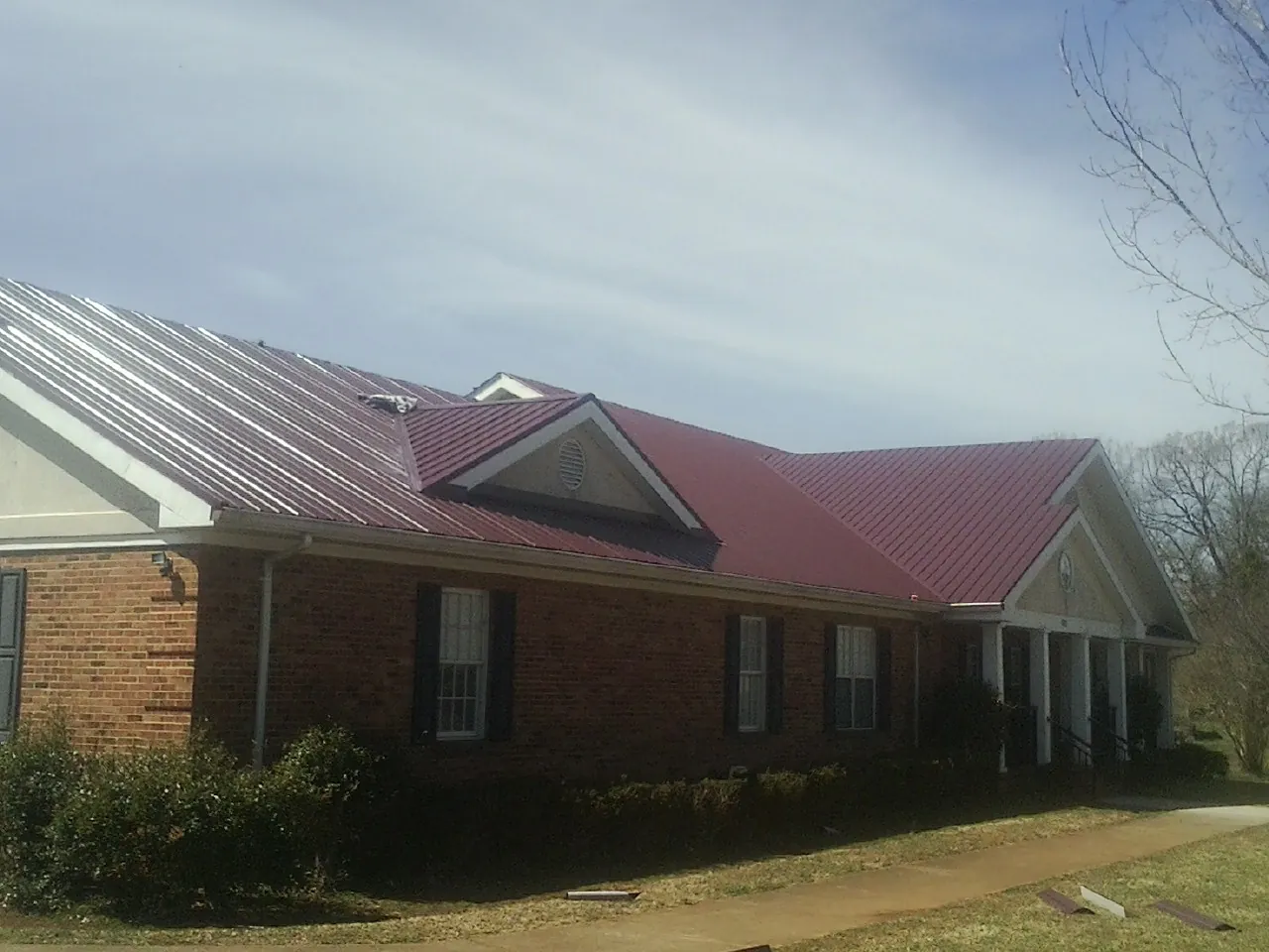 Red metal roof with gabled entries on a long brick building, from a Hail Damage Roof Repair job in Zwingle