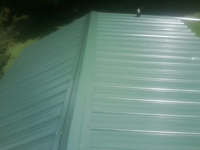 New green metal panels meeting at the ridge of a roof — Flat Roof Repair work by our crew in Zwingle