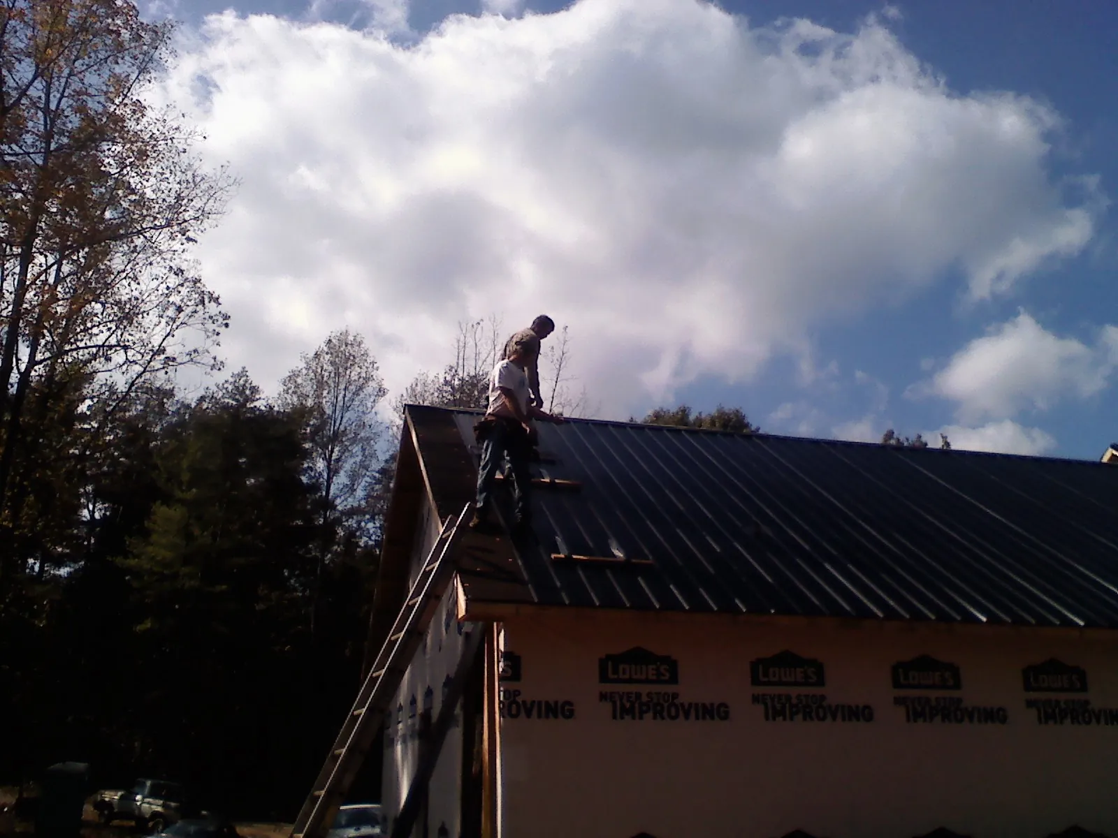 Roofer fastening dark metal panels high against a cloudy sky, from a Roof Inspection job in Zwingle