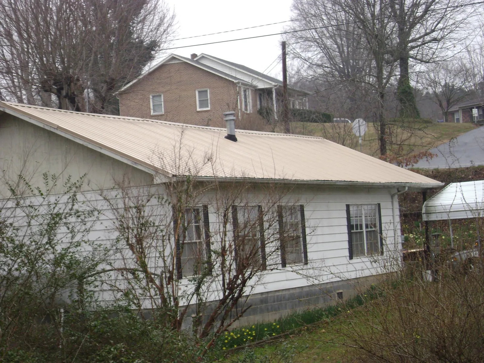 Tan metal roof on a white sided house set into a hillside — Commercial Roofing by Roofing Brothers in Zwingle